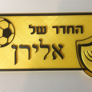 שלט דלת תלת-ממדי בצבע צהוב עם אותיות וסמלים בולטים בשחור, בעיצוב כדורגל ומנורה עם הכיתוב החדר של אלירן