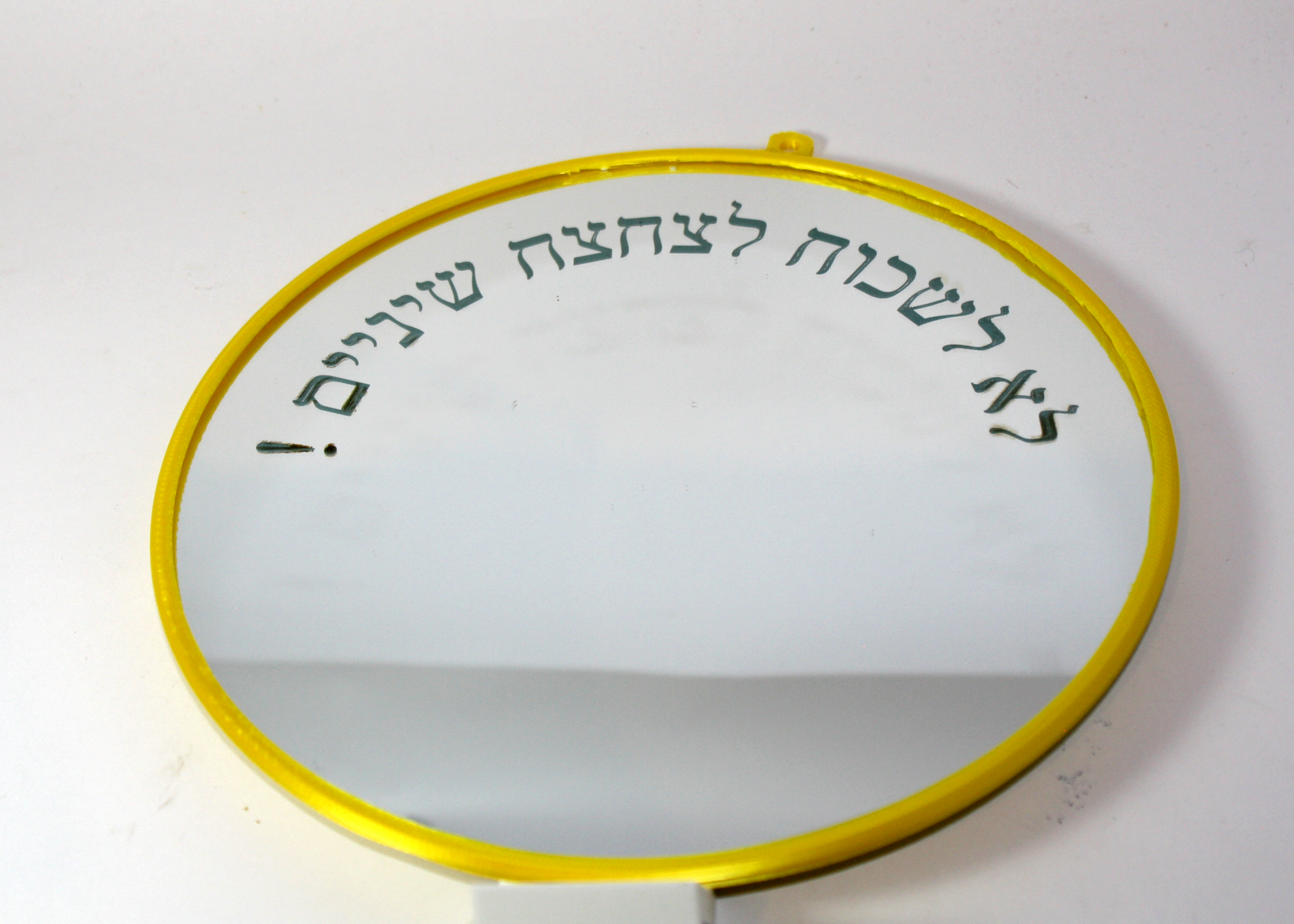מראה עגולה בקוטר 20 ס"מ עם מסגרת וחור תלייה מובנה, ועליה חריטת לייזר מעוגלת של כיתוב מותאם אישית בצבע לבן נקי, מונחת על רקע קיר אמבטיה